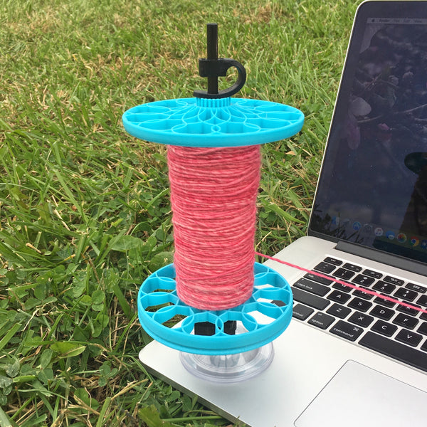 SimpleKate mounted to a laptop, holding a bobbin for yarn dispensing, TensiTamer engaged.
