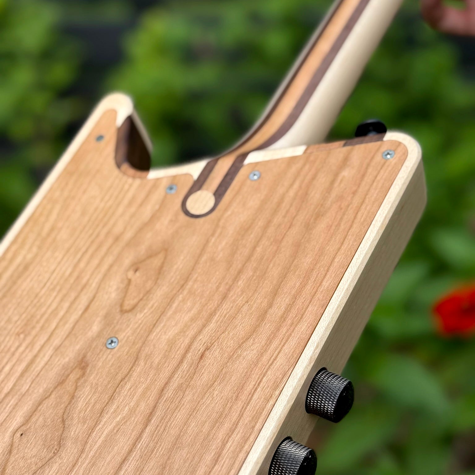 Close-up of the back of a custom-solid-body electric ukulele, showing wood grain, knobs, fasteners.
