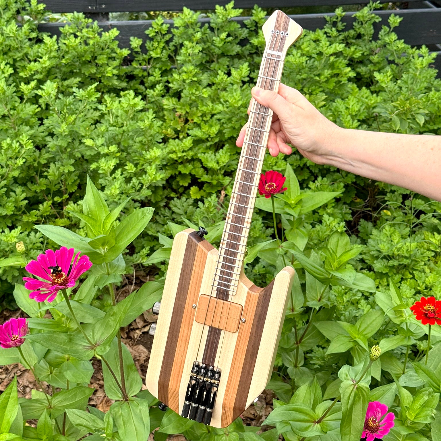 Custom solid-body headless electric ukulele being held in a garden.