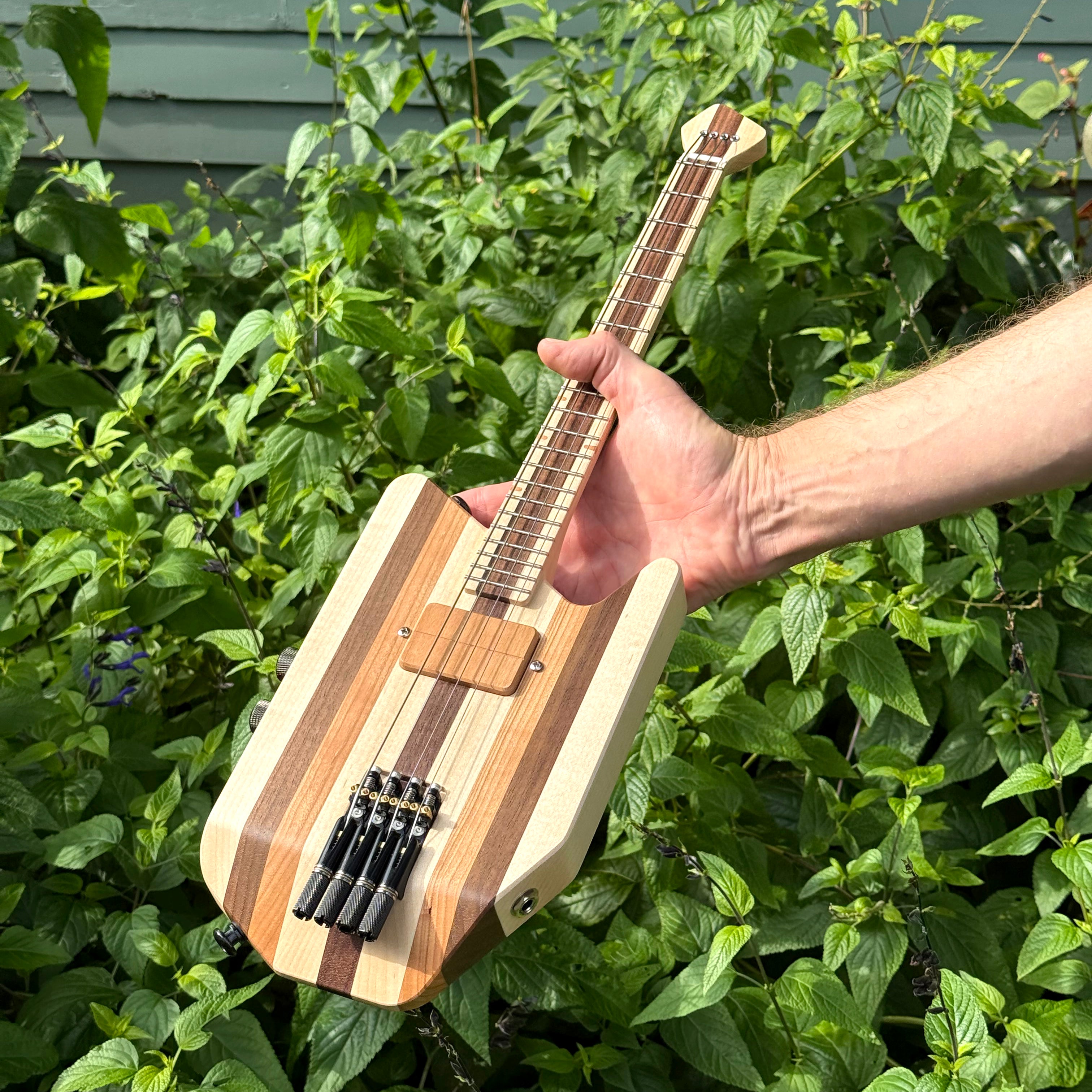 Custom solid-body headless electric ukulele being held in a garden.
